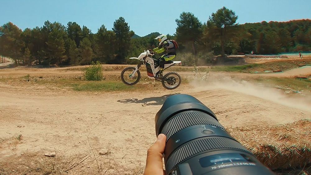 Osoba jadąca motocyklem w powietrzu, z obiektywem kamery na pierwszym planie. Motocyklista jest ubrany w biało-czerwony strój i żółty kask.
