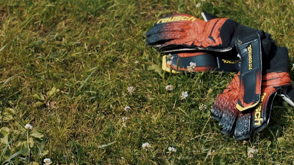 Para pomarańczowo-czarnych rękawic bramkarskich leży na trawie.